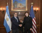 Argentine Ambassador shaking hands with young man with Argentine and US flags in background